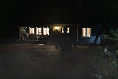 Silhouette demon in front of illuminated cabin at night