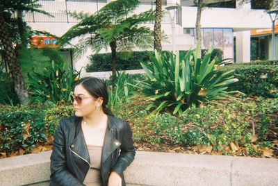 Young woman wearing sunglasses while leaning on railing against plants