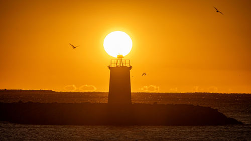 Lighthouse by sea against sky during sunset