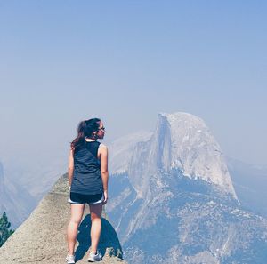 Rear view of young woman standing on mountain against clear sky