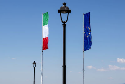 Low angle view of italian and european union flags against blue sky