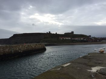 Scenic view of town by sea against cloudy sky