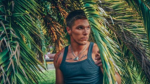 Portrait of young man standing on palm tree