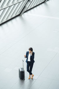 Female entrepreneur with suitcase talking on mobile phone while standing at corridor