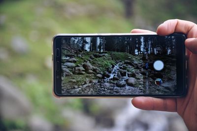 Cropped hand photographing stream with mobile phone in forest