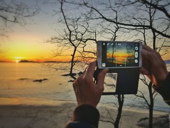 Close-up of hand holding mobile phone at sunset