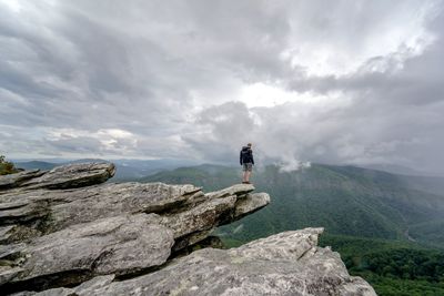 Rear view of male hiker standing on mountain against cloudy sky