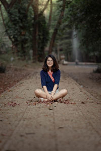 Portrait of smiling young woman sitting on footpath in forest