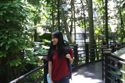 Smiling woman looking at plants while standing on footbridge