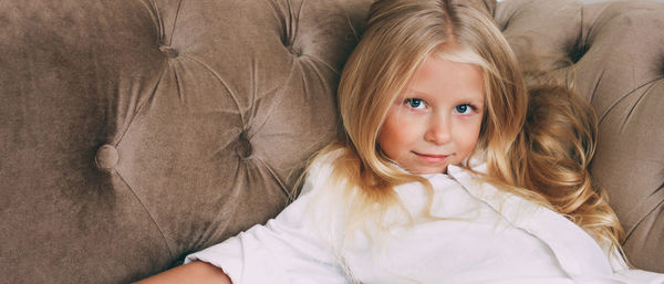 Beauty fashion portrait of little tween girl with fair long hair in white shirt on beige sofa 