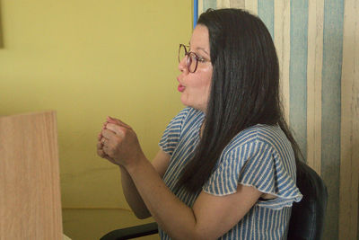 Side view of young woman sitting against wall at home