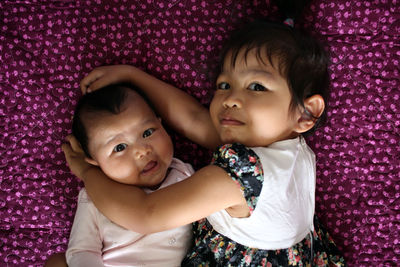 High angle portrait of sisters lying on bed at home