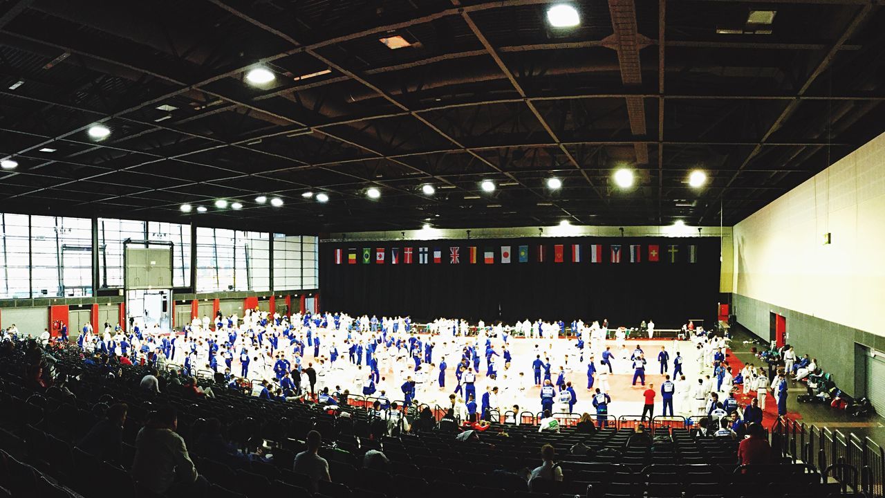 large group of people, illuminated, indoors, crowd, lighting equipment, night, men, person, ceiling, lifestyles, arts culture and entertainment, leisure activity, built structure, hanging, stadium, architecture, abundance, in a row