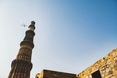 Low angle view of qutb minar against airplane flying in clear sky