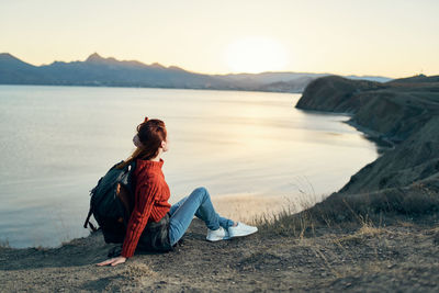 Man sitting on rock at beach against sky during sunset