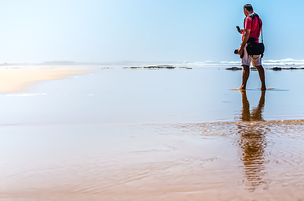 MAN STANDING ON SHORE AGAINST SKY