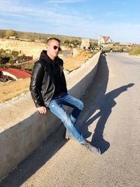 Young man sitting on retaining wall against sky