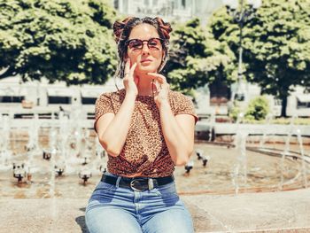 Portrait of young woman wearing sunglasses sitting against fountain