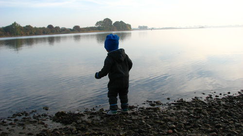 Rear view of boy standing at beach against sky