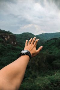 Cropped hand of person against mountain and sky