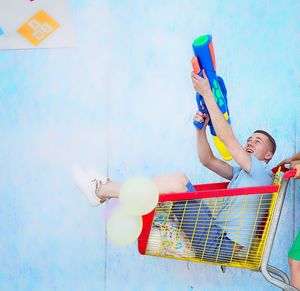 Man aiming with squirt gun while sitting in shopping cart by wall