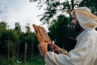 Side view of beekeeper examining beehive