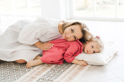 Mother and her little daughter are lying on a pillow on the floor, spending their free time together