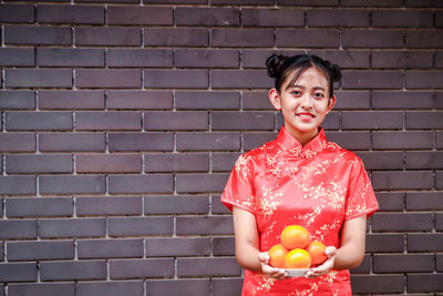 Portrait of smiling woman standing against brick wall