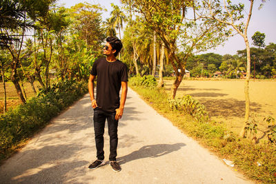 Full length portrait of young man standing on road against trees