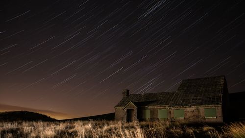 House on field against star trails