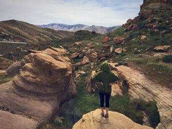 Rear view of woman standing on cliff against sky