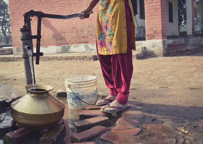 Low section of woman taking water from tubewell