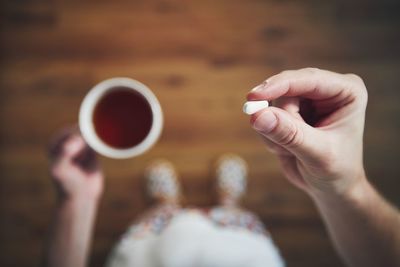 Sick young man in nightwear is taking pills and drinking hot tea..