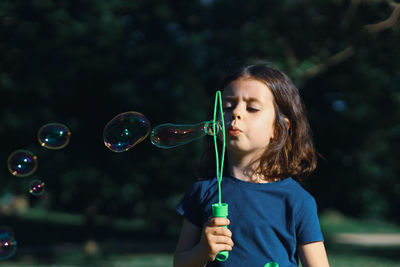 Portrait of a beautiful caucasian girl blowing soap bubbles while standing in a park