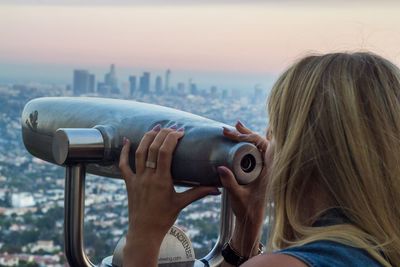 Woman looking through coin-operated binoculars against sky during sunset