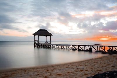 Pier on beach against sky during sunset