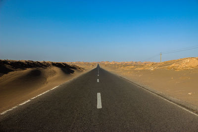 Empty road amidst desert against clear sky