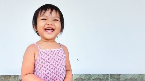 Cute happy girl standing against white wall