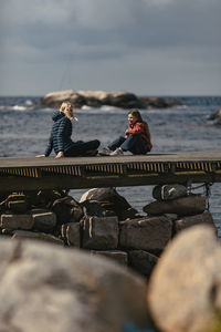 People sitting on rock by sea against sky