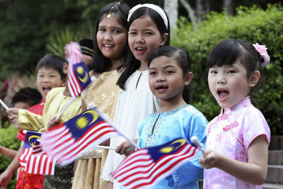 Cheerful friends holding malaysian flags while standing at park