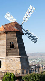 Traditional windmill by building against clear sky