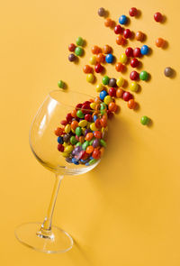 Colorful candies in a wine glass on yellow background