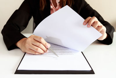 Midsection of woman holding paper while sitting on table