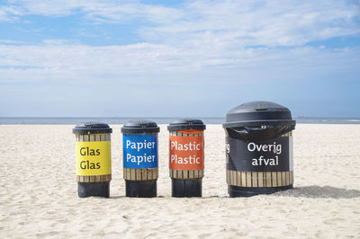 Recycling trash cans on beach against sky