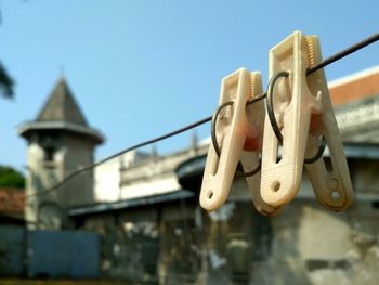 Low angle view of clothespins hanging on rope against buildings and sky
