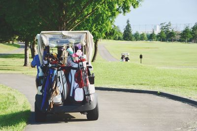 Golf clubs hanging on cart over road against trees