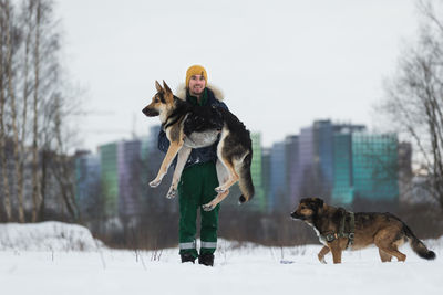 Portrait of man carrying dog on snow covered land against sky
