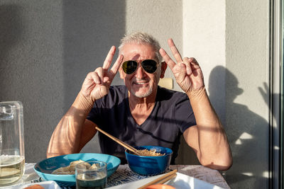 Attractive middle-aged man have fun while eating sitting on table laid chinese food in front of wall