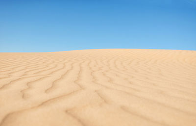 Sand dunes in desert against clear blue sky