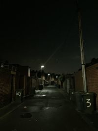 Illuminated street amidst buildings against sky at night